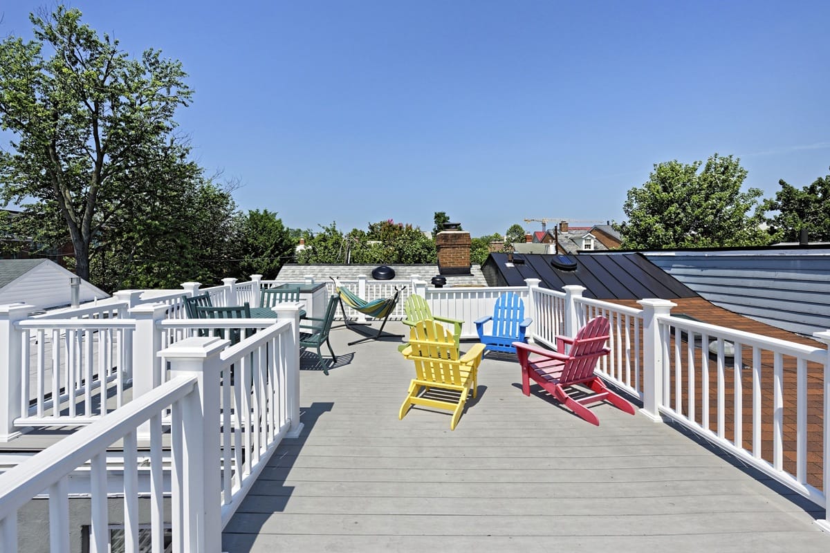 Rooftop deck with white railings and colorful Adirondack chairs (yellow, blue, pink, red) under a clear blue sky.
