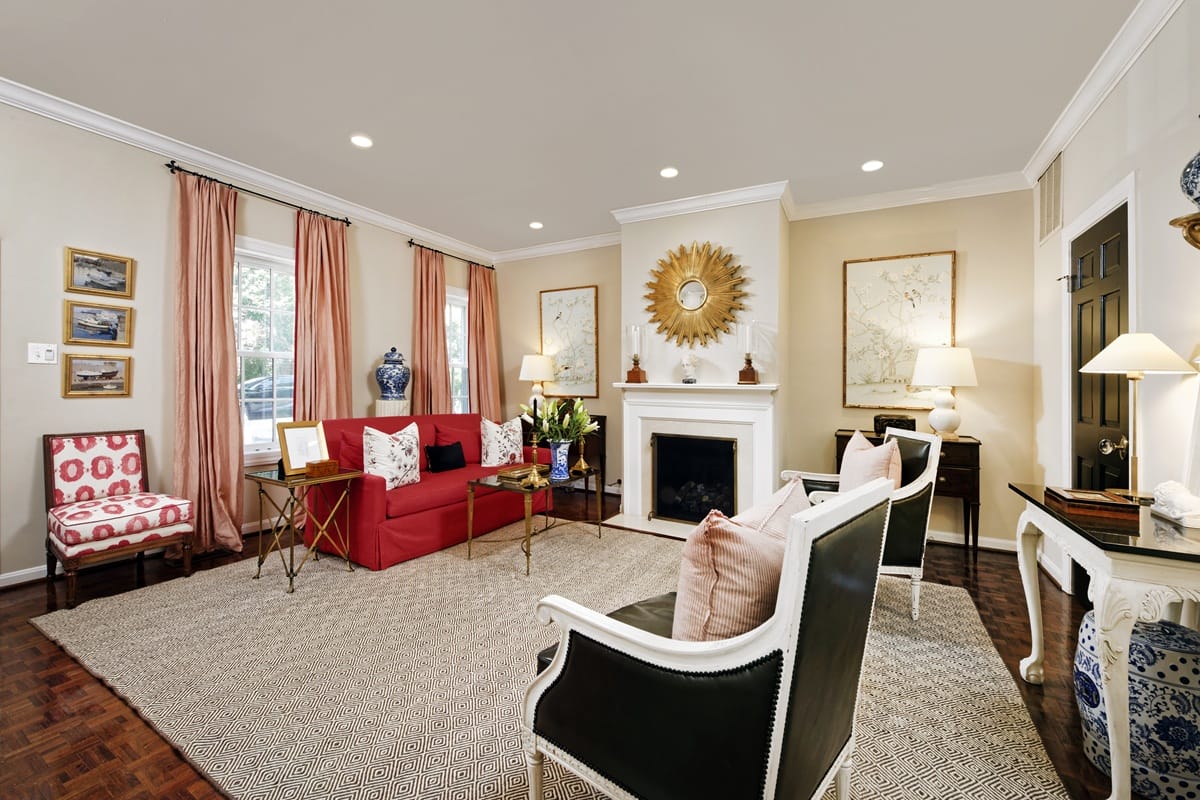Elegant living room with a red sofa, pink curtains, fireplace with a sunburst mirror, and cream/black chairs.