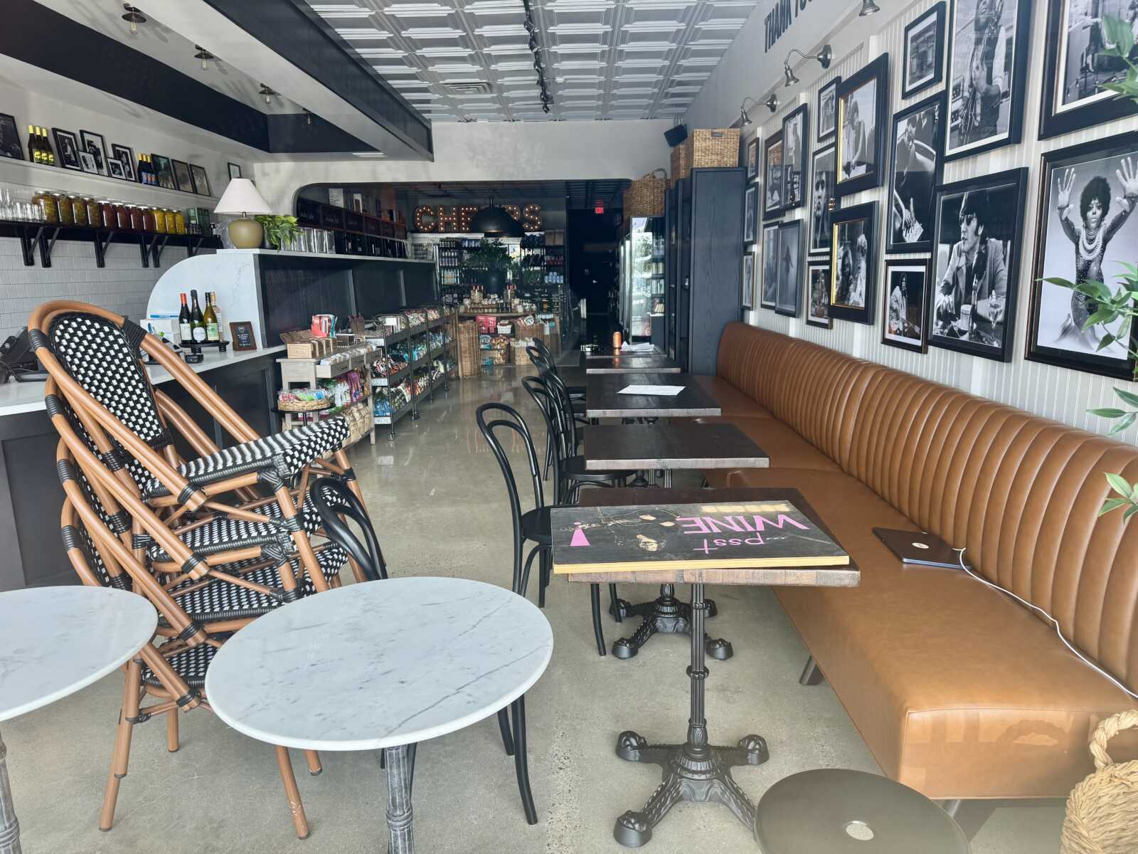 Long brown leather banquette runs along the wall with black tables and a gallery of black-and-white framed photos; shelves and drinks area to the left.