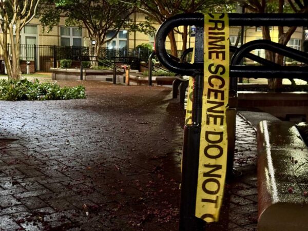 Yellow crime scene tape wrapped around a black railing in a wet courtyard at night, cordoning off the area.