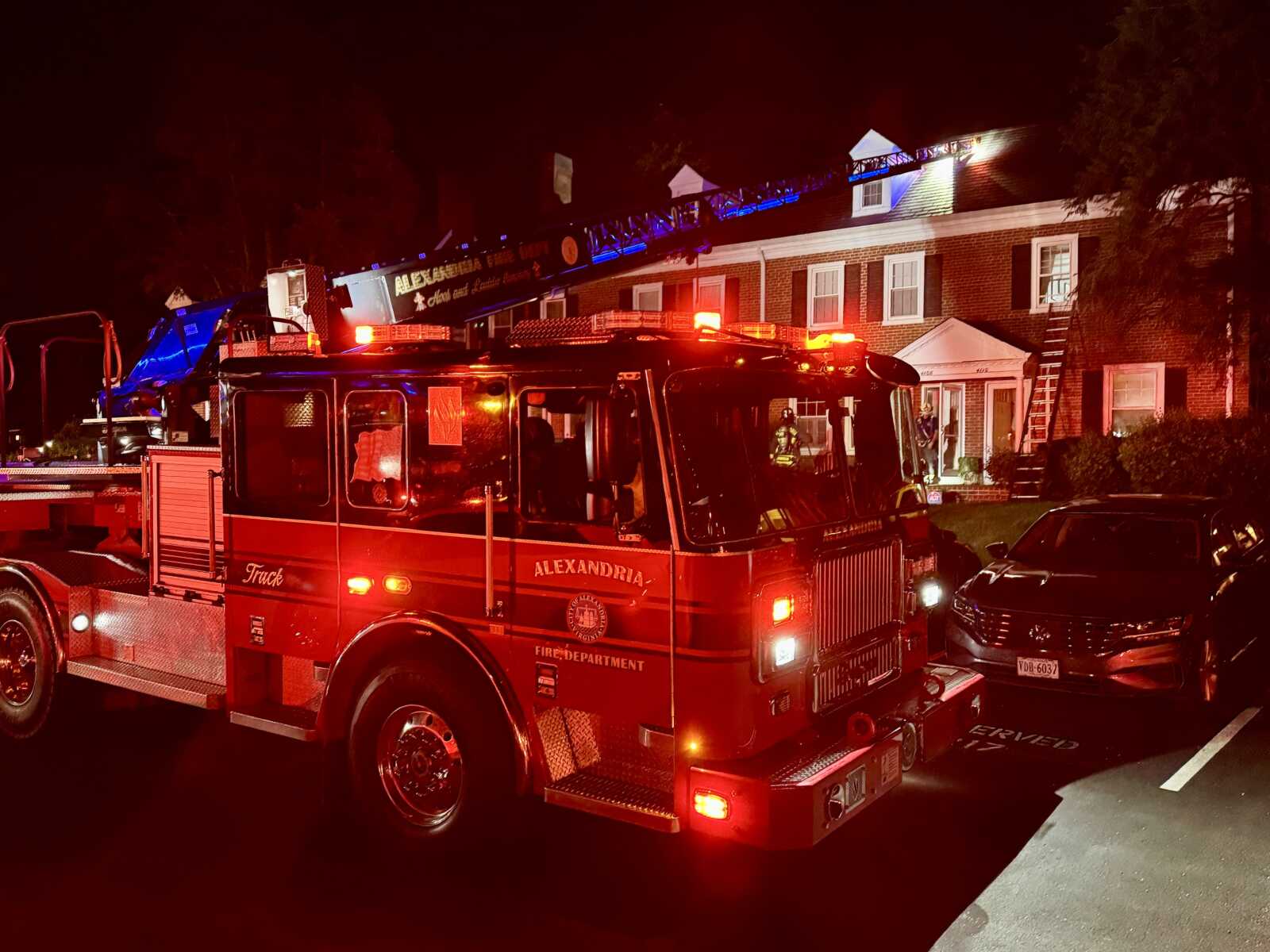Red fire engine with extended ladder responding to a house fire at night, flashing emergency lights illuminating the scene