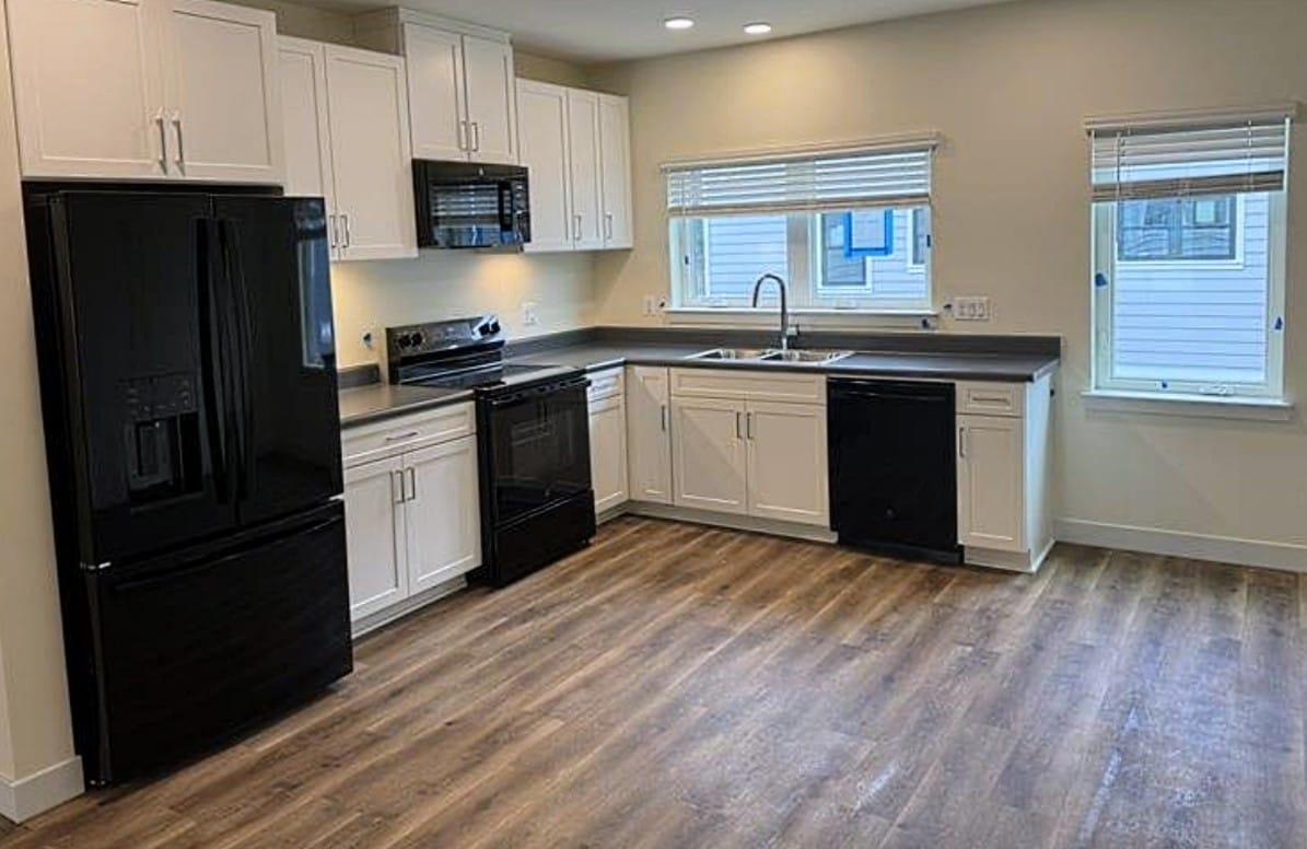 Modern kitchen with white cabinets, black appliances, gray countertops, and wood-look flooring.