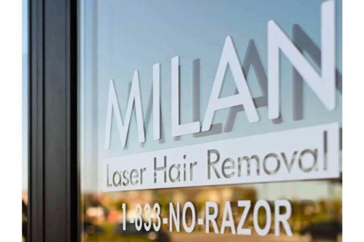 Glass storefront window with 'MILAN' sign and 'Laser Hair Removal' text, advertising contact number 1-833-NO-RAZOR