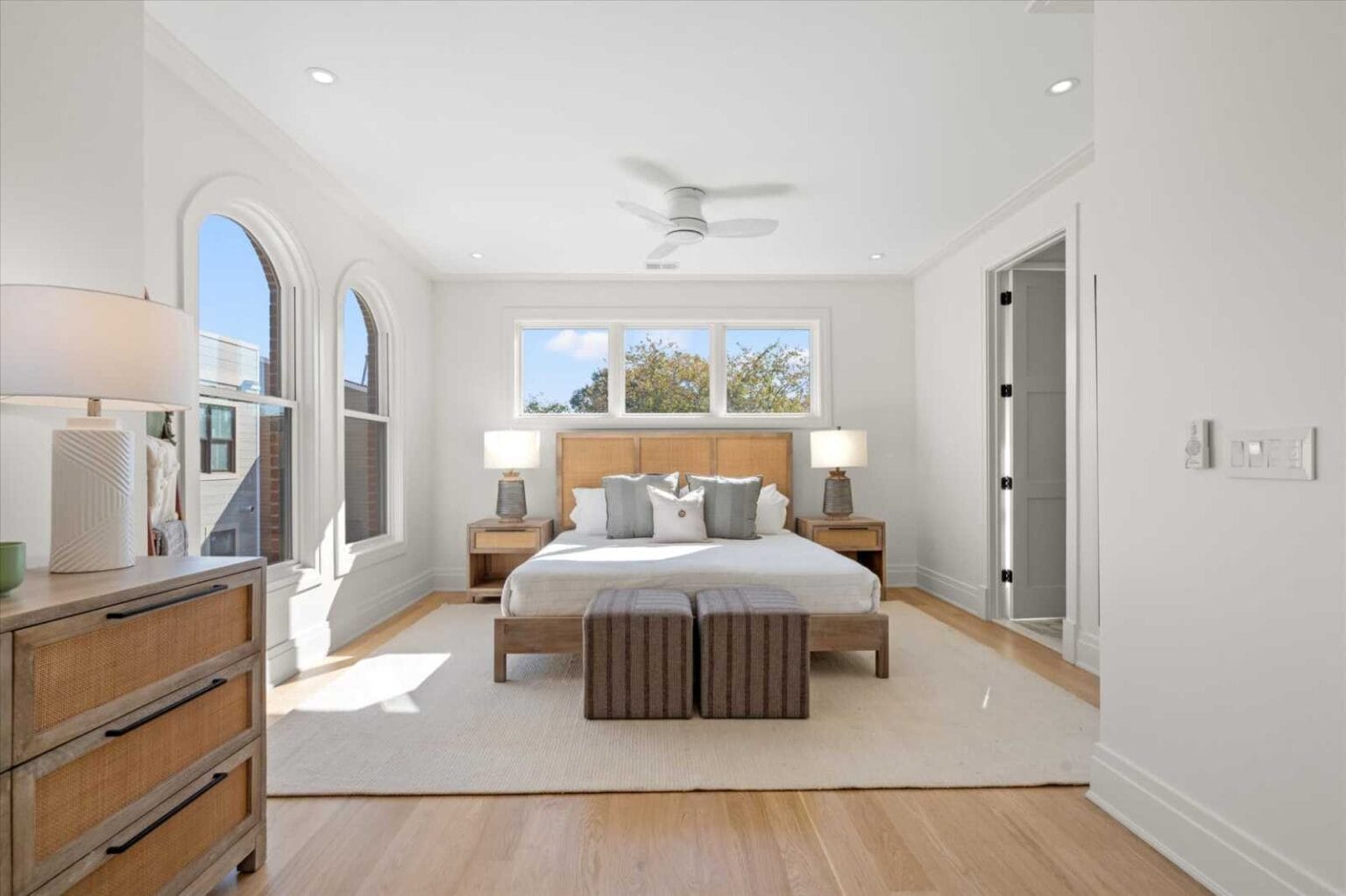 Bright master bedroom with arched windows, a wooden headboard bed, two nightstands, and pair of lamps filling the space with natural light.