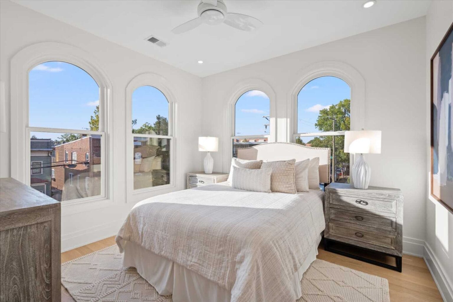 Bright bedroom with four arched windows, white walls, and a gray-washed bed with two matching nightstands.
