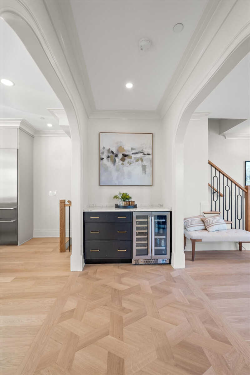 Modern open-space kitchen nook with a black drawer cabinet, a glass-front wine cooler, marble countertop, and a framed abstract painting above.