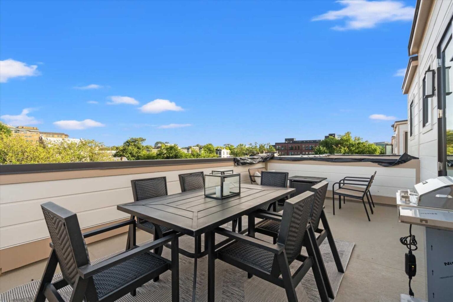 Rooftop patio with a dark dining table and eight chairs under a bright blue sky.