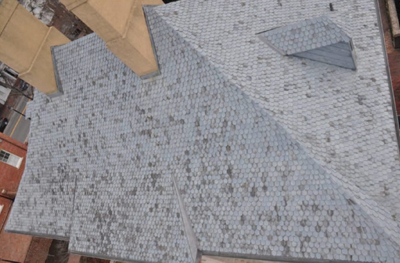 Aerial view of a large grey roof with many small circular shingles arranged in a pattern and intersecting slopes.
