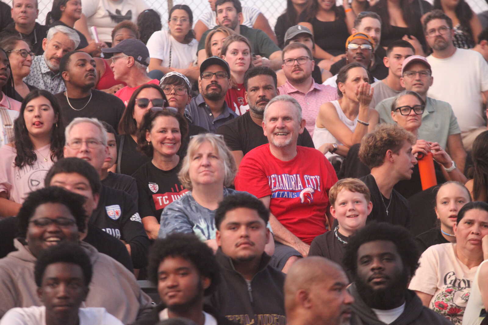 Crowd of diverse spectators sitting in bleachers at an outdoor event that's likely a performance or game.