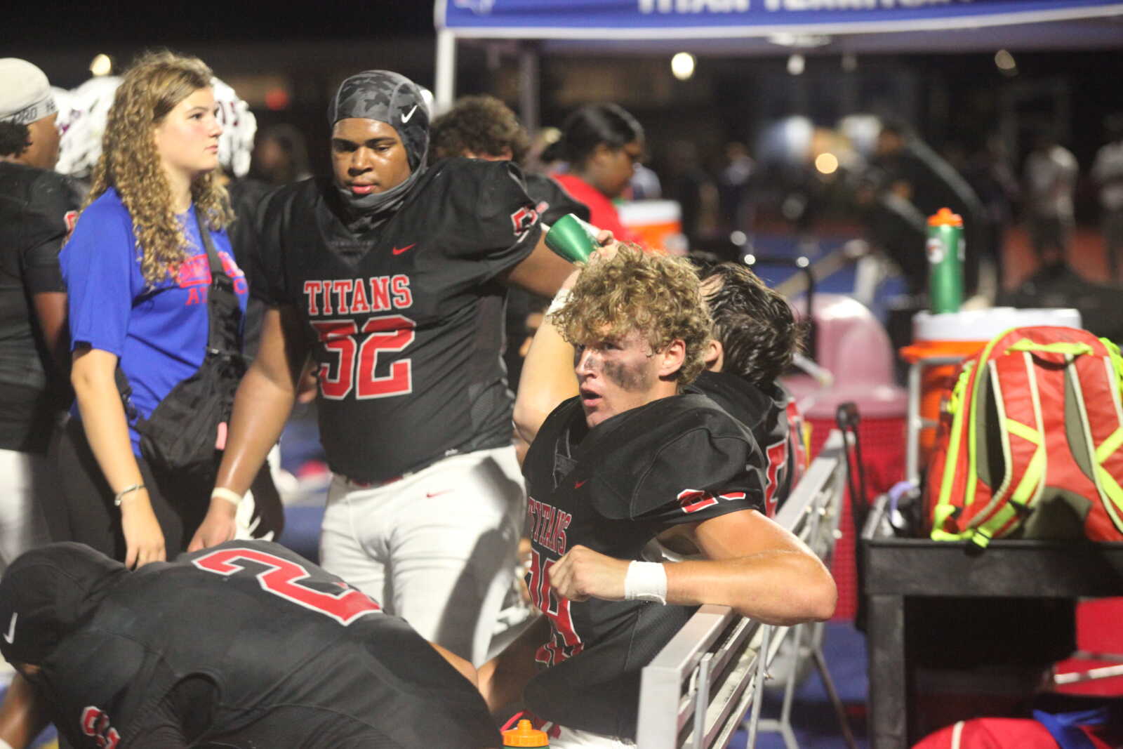 Football players in black Titans uniforms celebrate on the sideline with a teammate ducking onto a bench area, girl in blue watching nearby