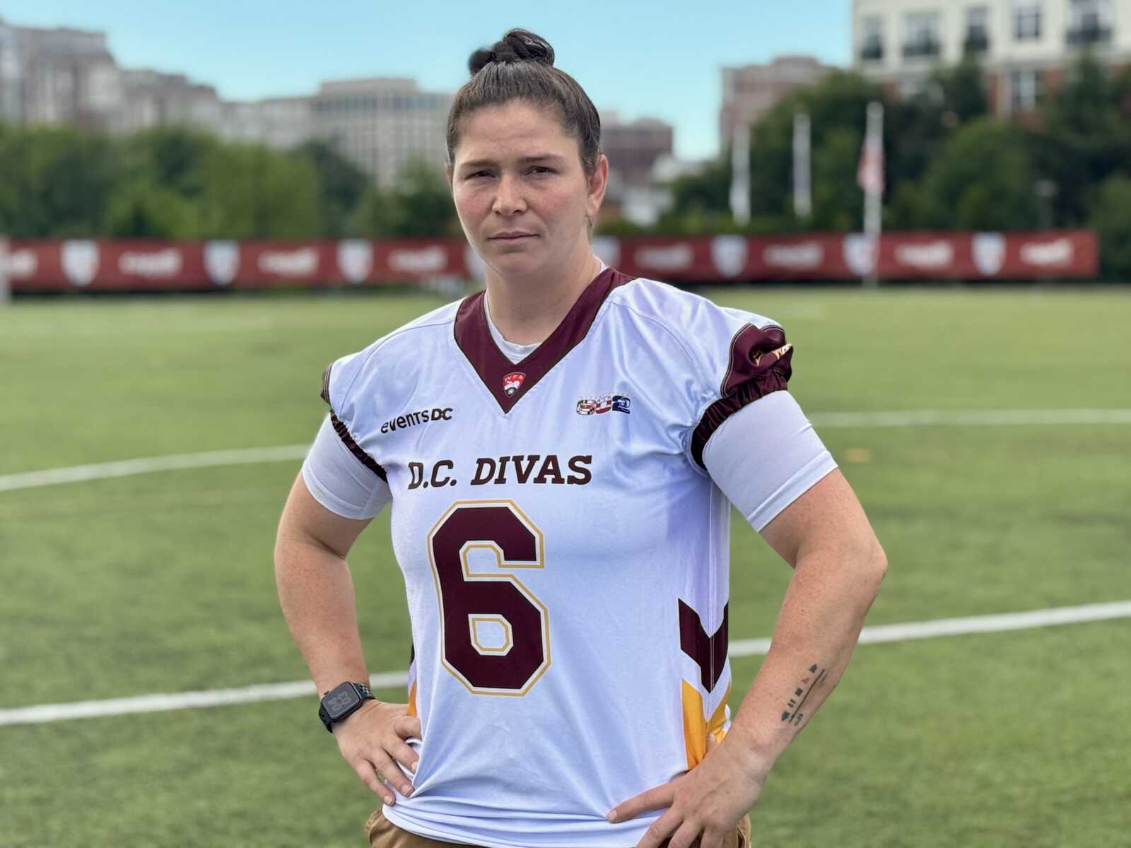 Female athlete in a white DC Divas jersey with number 6, standing with hands on hips on a green sports field.