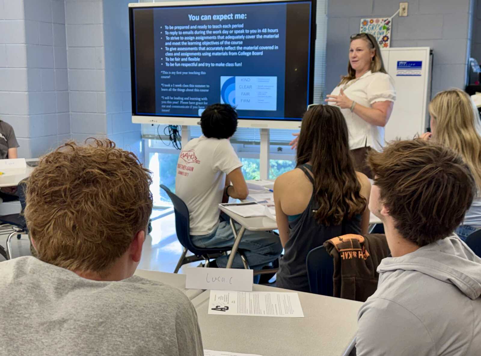 Teacher standing beside a large screen presenting to students in a classroom