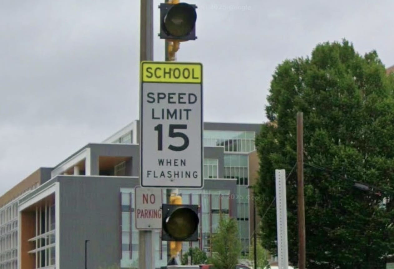 Screenshot | ALXnow School zone sign indicating 15 mph speed limit when flashing, with traffic light and street scene in the background.