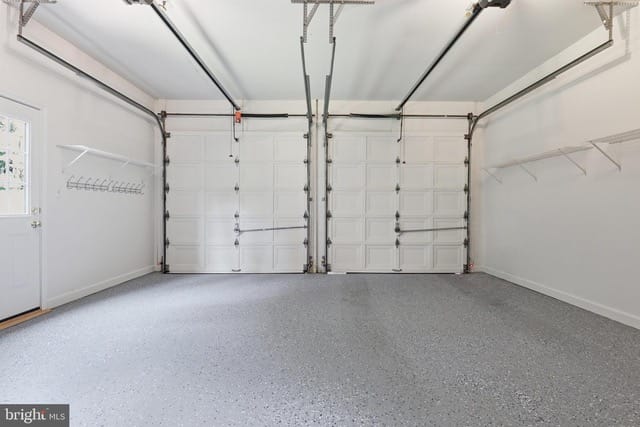 Two-car garage with white paneled doors, concrete speckled floor, and wall-mounted storage shelves.