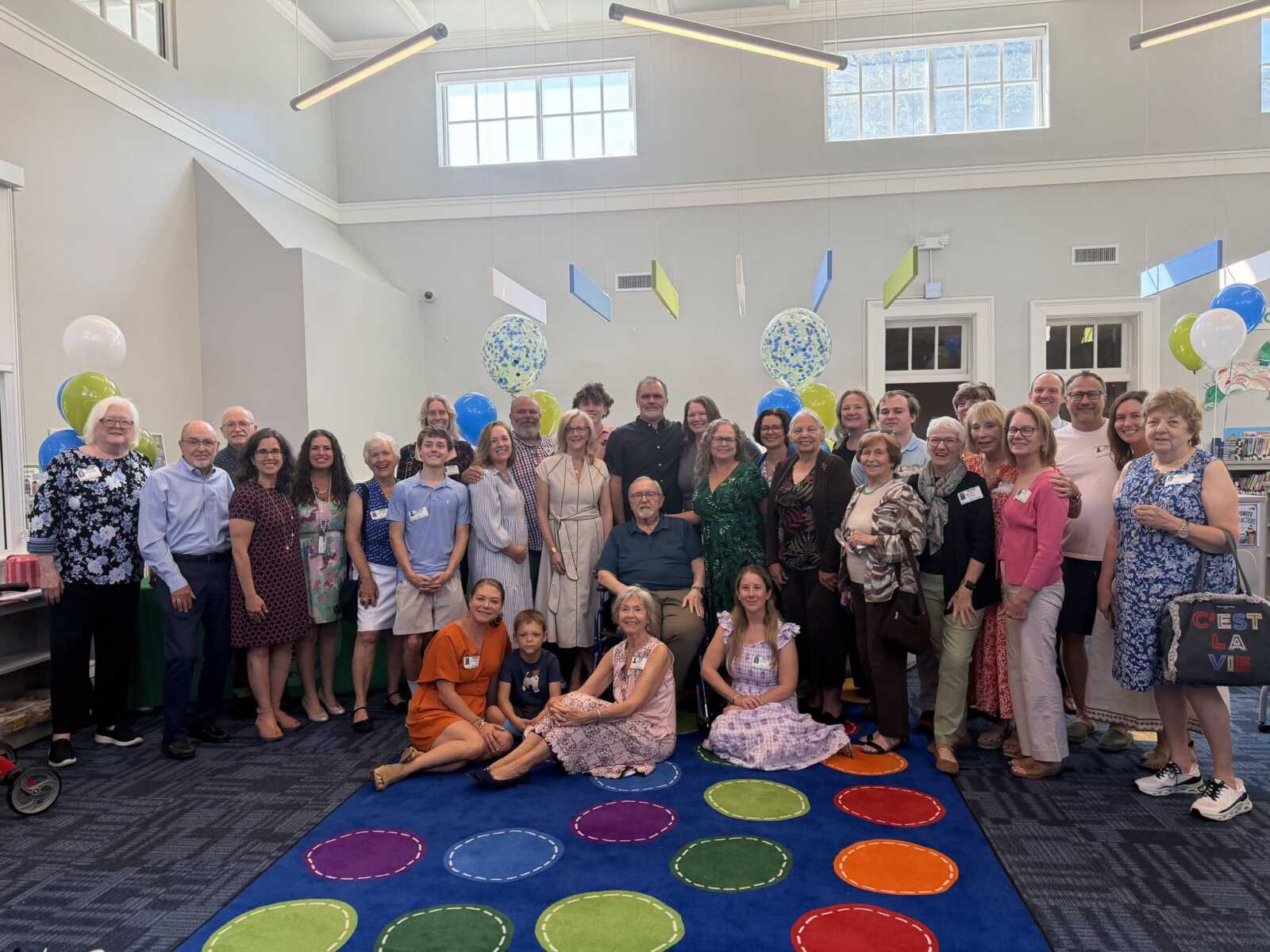 Group of diverse adults posing together for a celebration indoors, with balloons and colorful decor in a bright room.