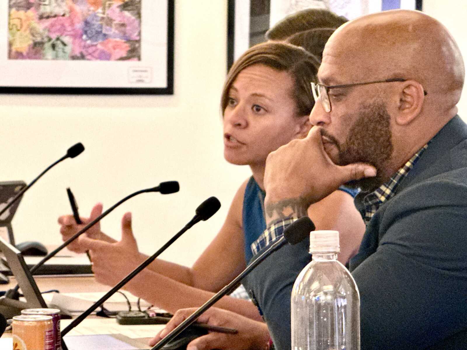 Two panelists speak into microphones during a discussion; woman gestures while man listens thoughtfully beside her.