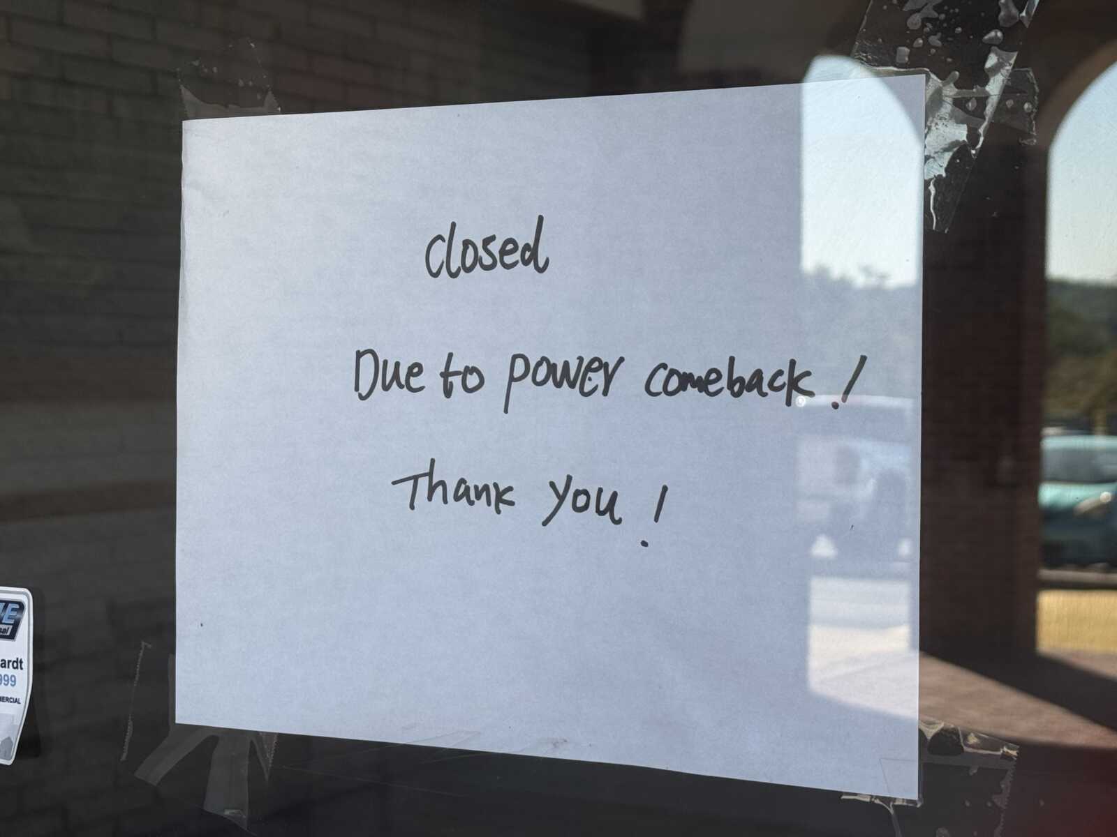 Sign on window stating the shop is closed due to a power outage, with 'Closed' and 'Thank you!' written in a casual font.