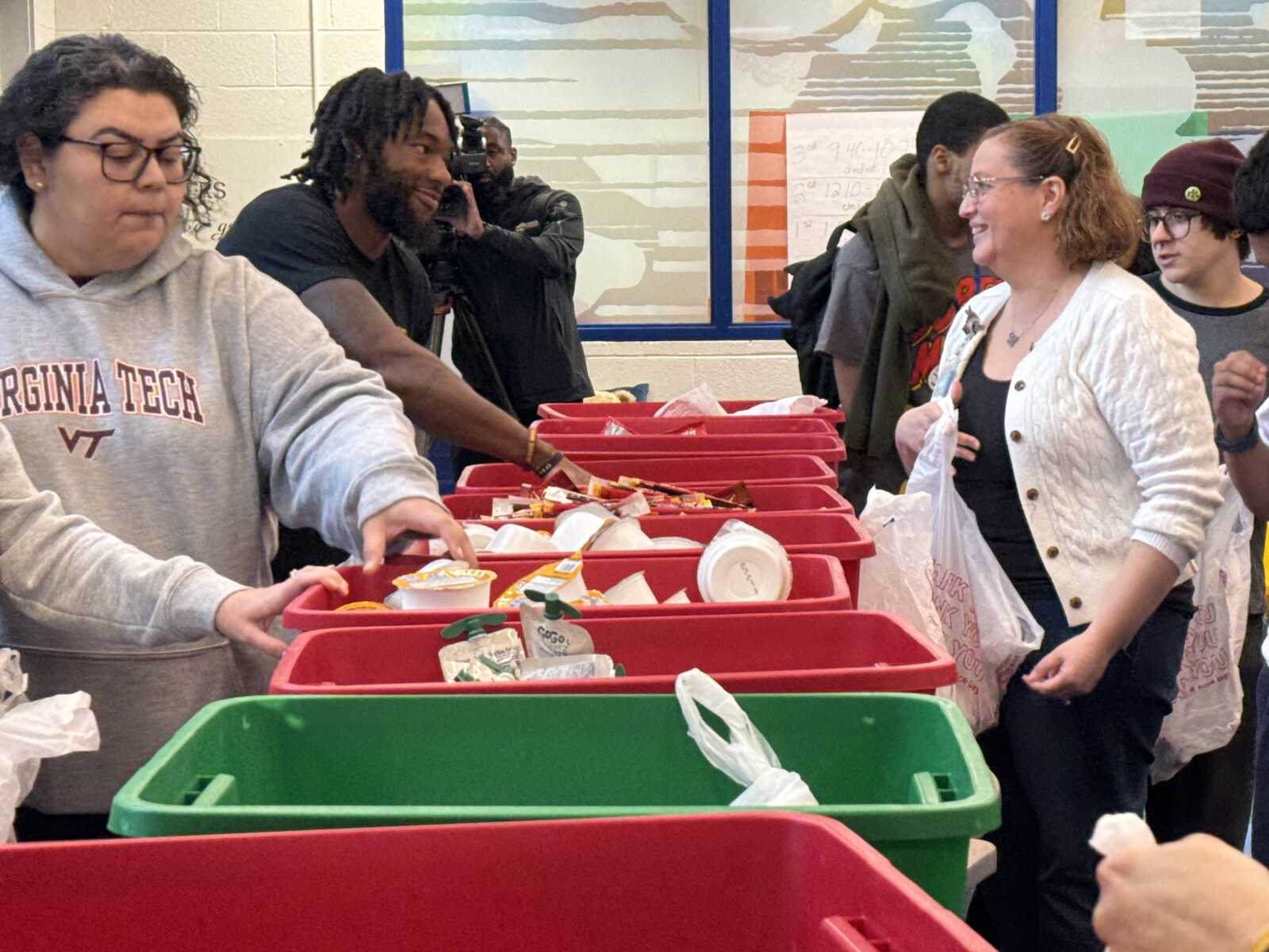 Volunteers sort canned goods and snacks into red donation bins at a food drive.