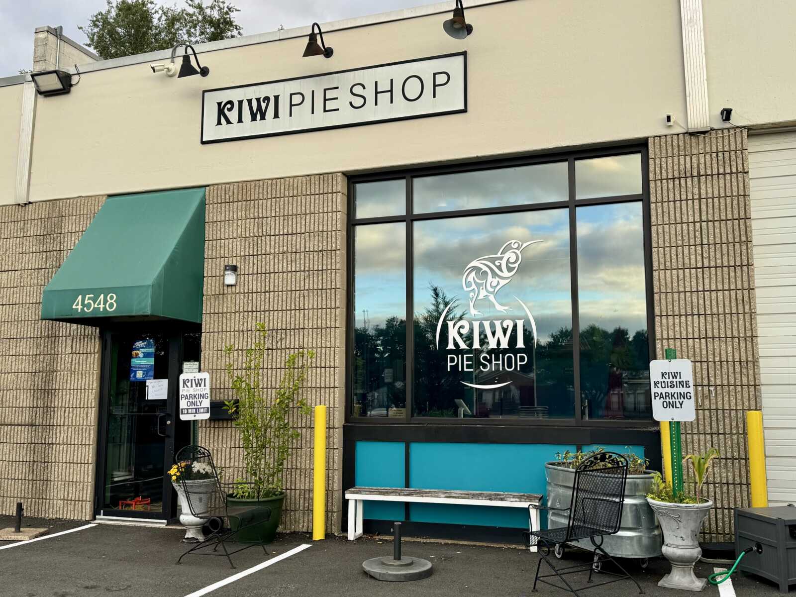 Front of Kiwi Pie Shop storefront with a green awning displaying the number 4548 and a large window featuring a white Kiwi Pie Shop logo.