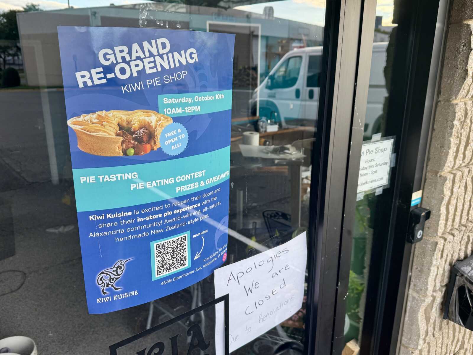 Blue poster on a store window announces the grand re-opening of Kiwi Pie Shop, featuring a pie image and event details (pie tasting, free entry).