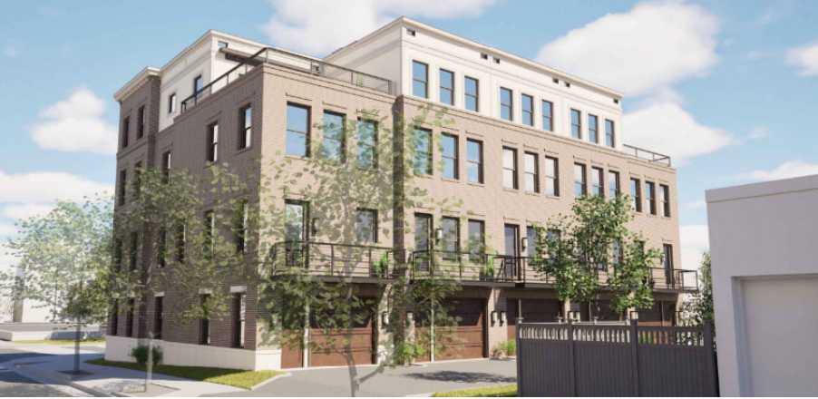 Three-story brick apartment building with balconies, trees along the sidewalk, and garage doors on the ground floor under a bright sky.