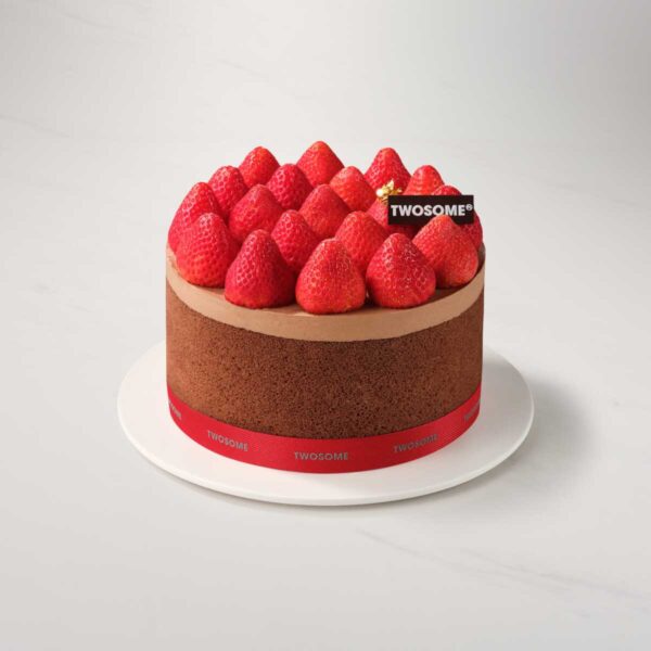 Round chocolate cake topped with neatly arranged strawberries and a small TWOSOME plaque on a white cake board.
