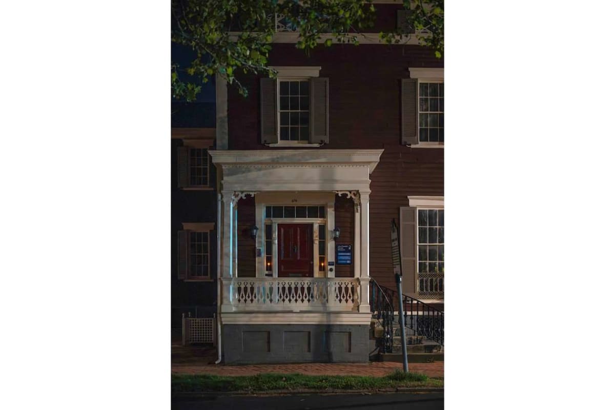 Two-story brick townhouse with a white decorative porch and red front door, lit at night