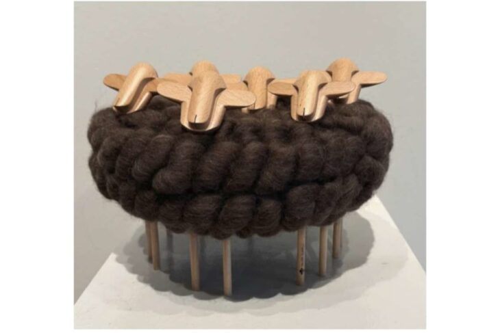 Dark brown chunky knitted ring on wooden dowel legs, topped with wooden clothespin shapes as a decorative sculpture.