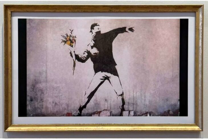 Framed street-art stencil of a man throwing a bouquet of flowers, in a gold frame.