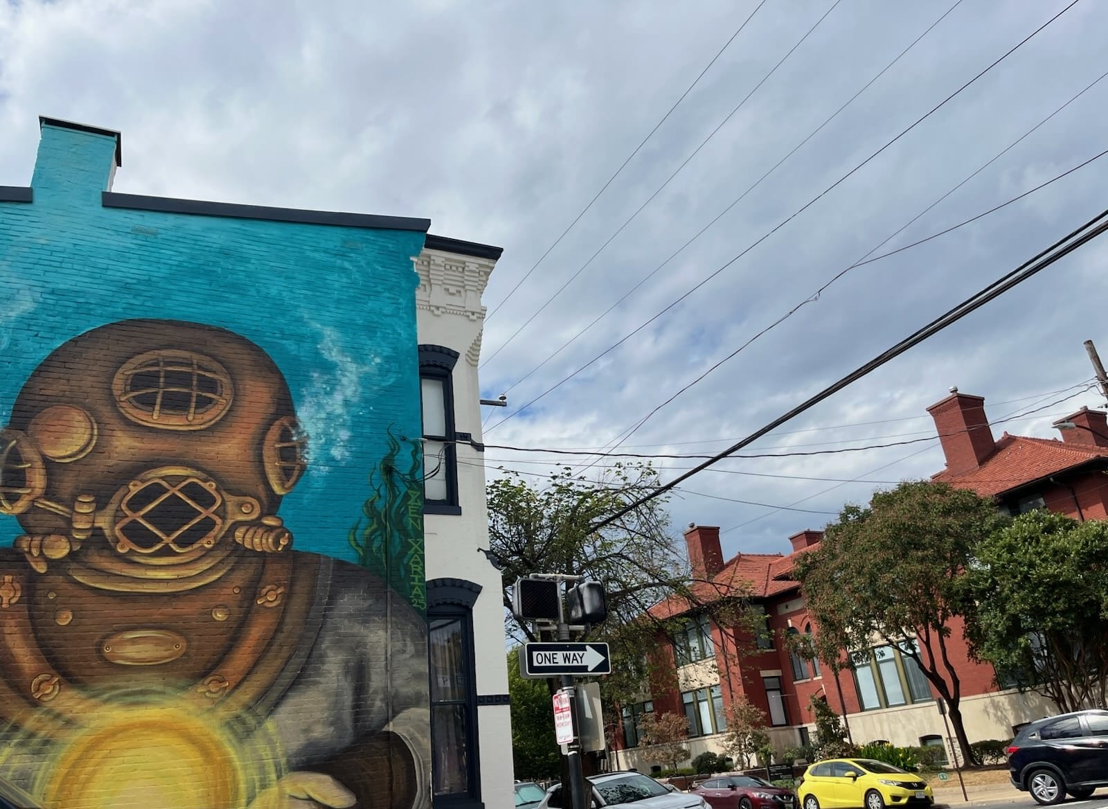 mural old town morning notes | ALXnow Mural of a vintage diving helmet on a bright turquoise wall beside a white building, with street and power lines nearby.