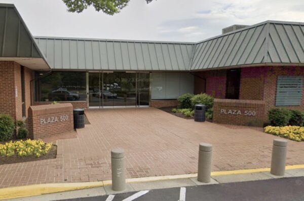 Exterior entrance to Plaza 500 with glass doors, brick walls, and a brick walkway lined by planters and trash cans.