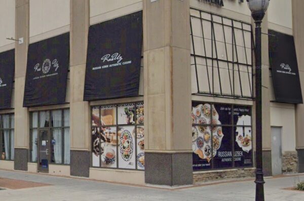 Storefront with tall beige columns and black banners advertising Russian Uzbek authentic cuisine, large window displays of food images, a street lamp in front.