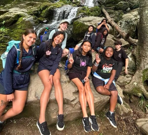 Group of kids sitting on mossy rocks beside a small waterfall in a forest, posing for a photo.