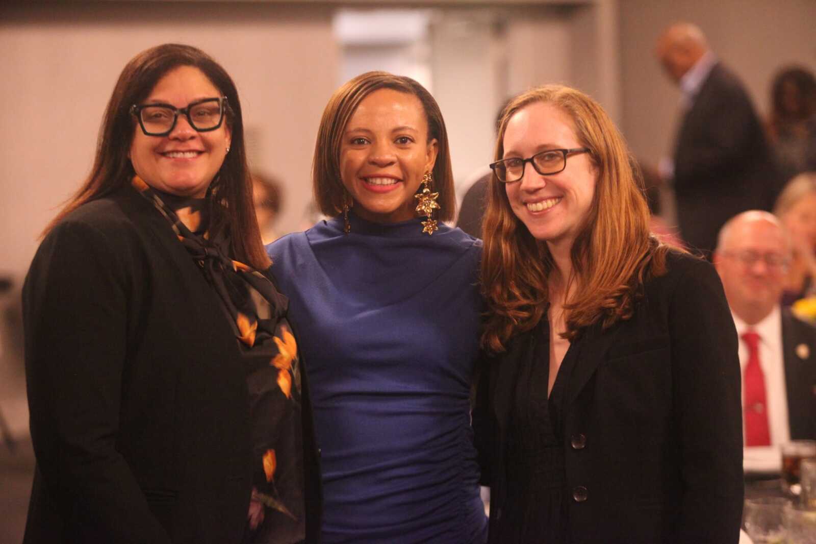 Three women posing together at a formal event, smiling for the camera.