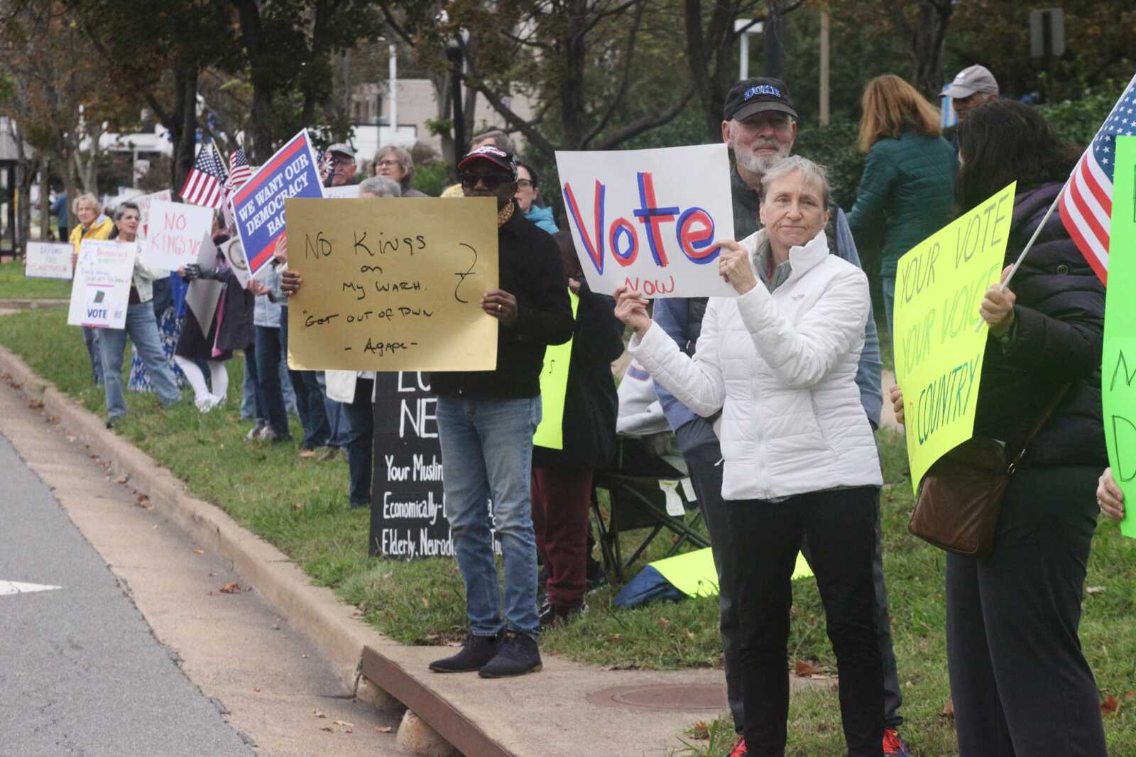 Group of protesters lined along a sidewalk holding signs and small American flags during a demonstration.