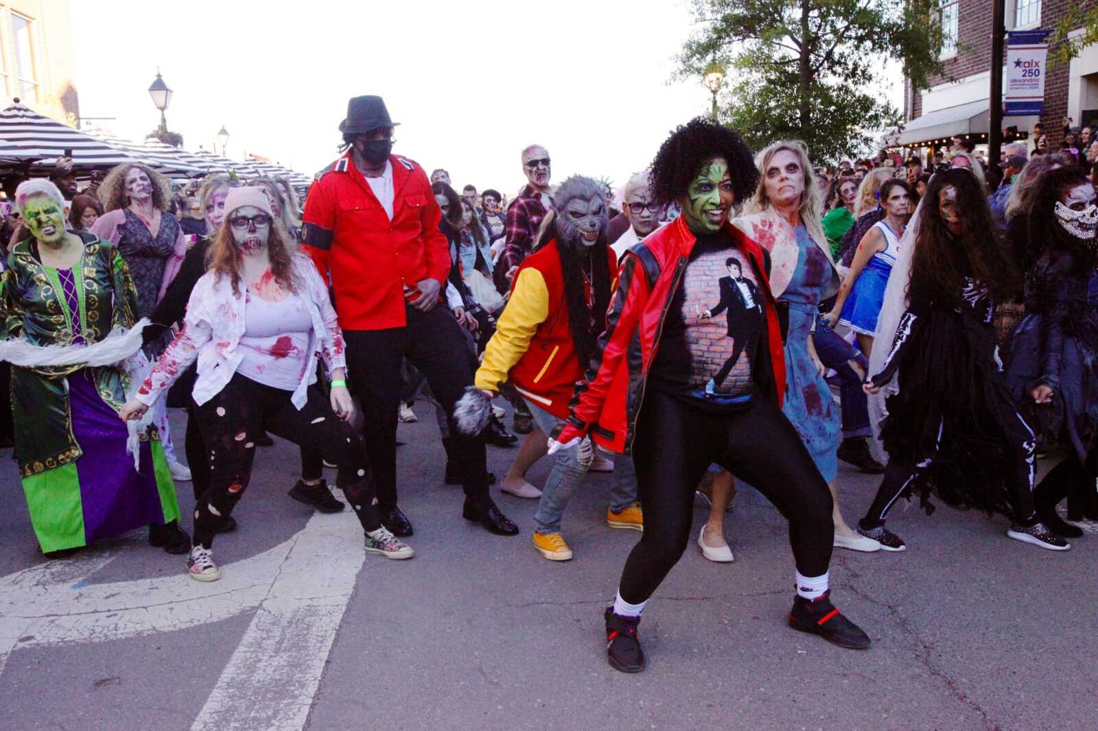 Crowd of people in Halloween costumes with zombie makeup marching down a city street during a parade, wearing colorful outfits and masks.