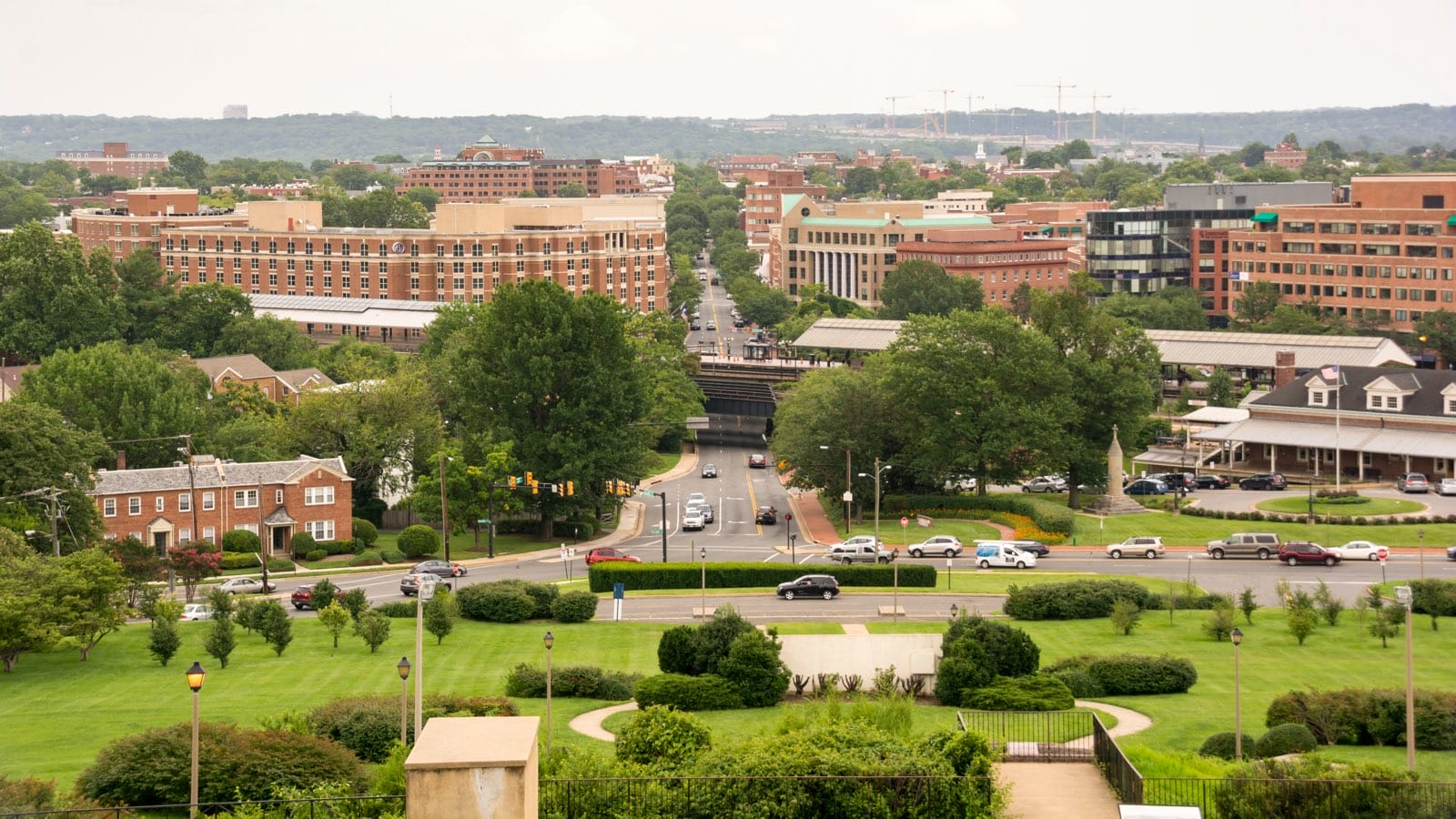Looking down King Street towards Old Town Alexandria and the Potomac River from the steps of the George Washington Masonic Temple (licensed via Adobe Stock) | ALXnow Aerial view of a city with a tree-lined central street, brick buildings, and a large green park in the foreground.