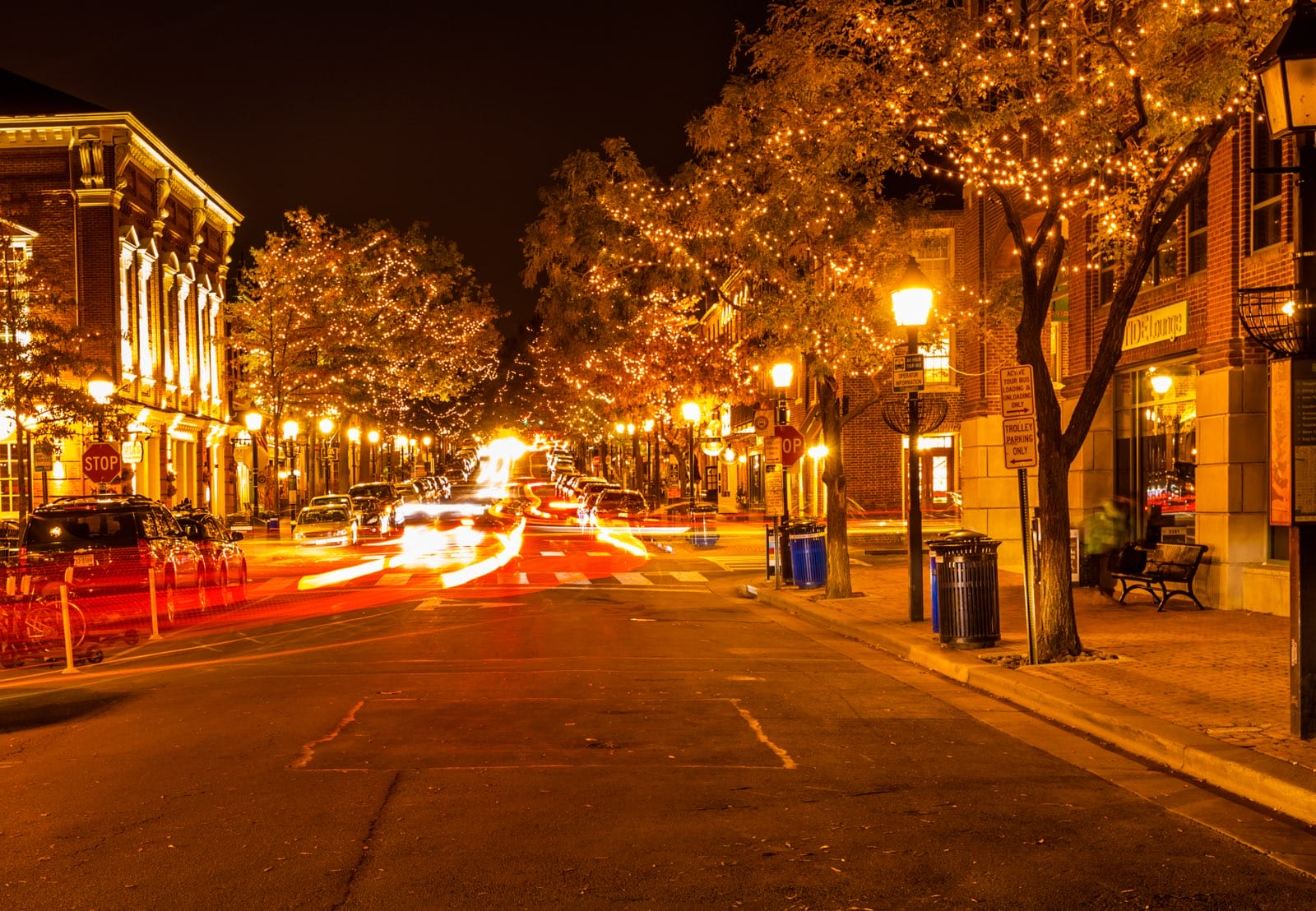 King Street in the Old Town Alexandria at night (licensed via Adobe Stock) morning notes | ALXnow Nighttime city street lined with warm string lights on trees and brick buildings, with blurred car lights and a quiet sidewalk scene.