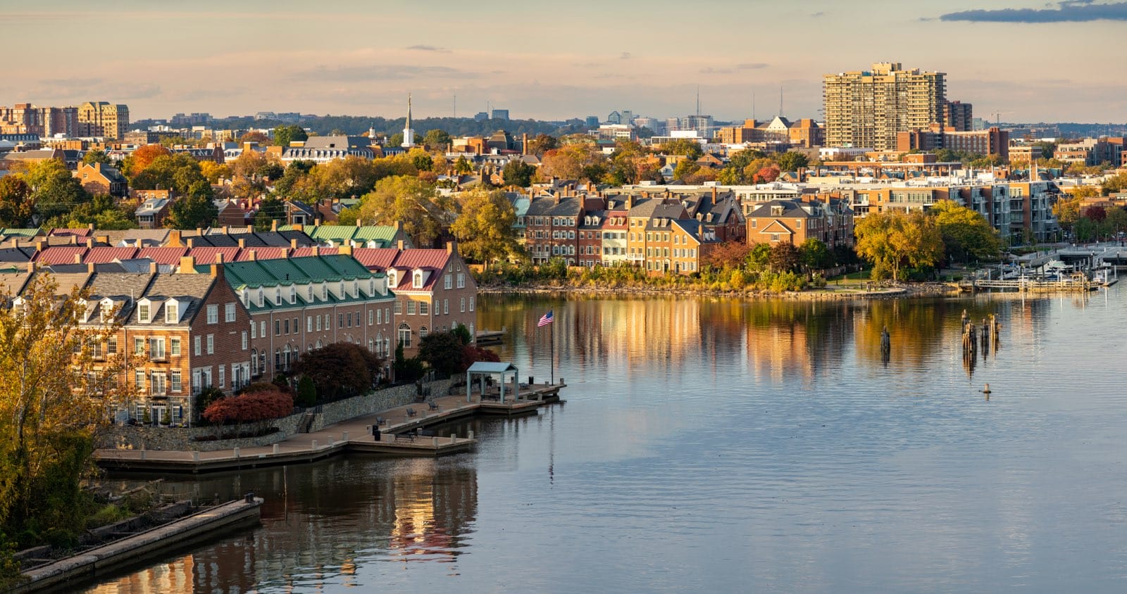 Modern townhomes in the historic city of Alexandria and the waterfront property along the Potomac River (licensed via Adobe Stock) morning notes | ALXnow A riverside city with brick townhouses, colorful autumn trees, and calm water reflecting the buildings at sunsetfall.