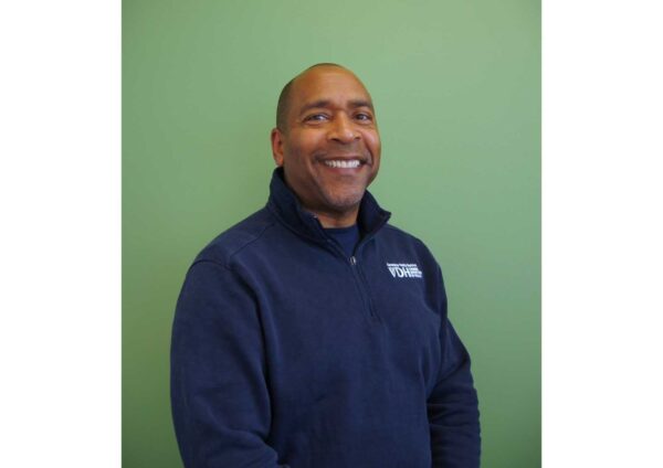 Smiling man in a navy fleece jacket posed against a green wall, looking at the camera.