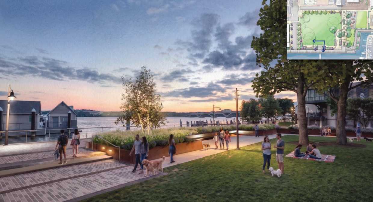 Sunset over a waterfront park with people walking, dogs, and picnics on a grassy lawn and brick pathways.