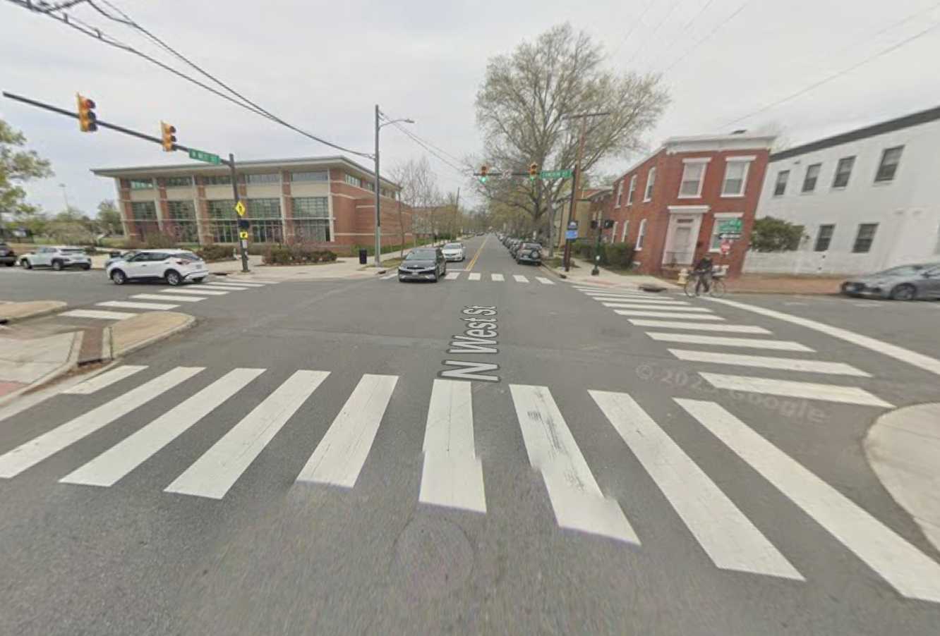 The intersection of Cameron Street and North West Street in Alexandria (via Google Maps) | ALXnow Intersection on N West St with wide striped crosswalks, brick building on the left and brick row houses on the right; cars on the road.