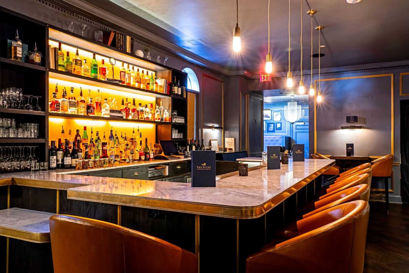 The Study at Morrison House bar (via The Study at Morrison House/Facebook) | ALXnow Luxurious bar interior with backlit bottles on open shelves, marble counter, and tan leather stools.