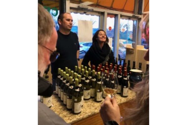 Group of people at a wine tasting around a counter lined with bottles of white wine on display.