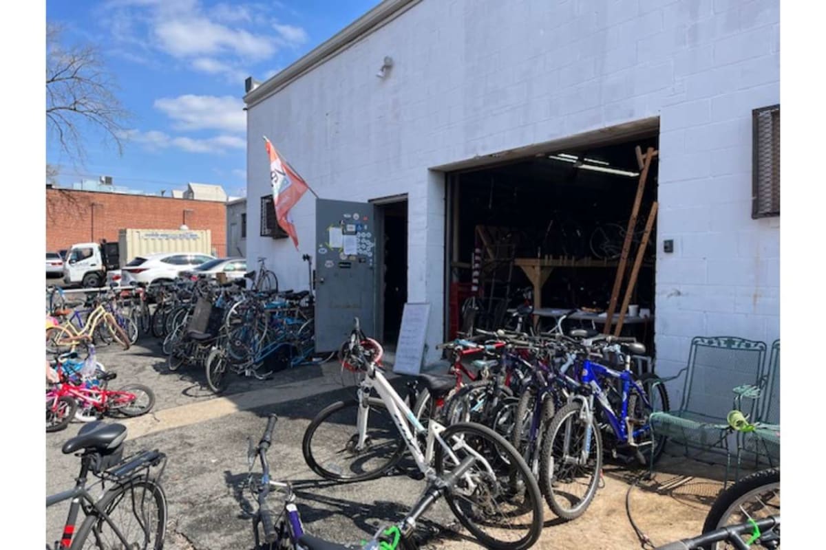 A bike shop exterior with numerous bicycles parked outside and a large open garage showing a workshop inside.