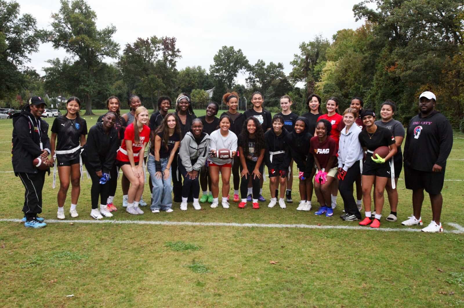 A diverse group of young athletes posing for a team photo on a grassy field, some with football gear and a ball in hand.