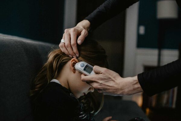Close-up of a person having a small electronic ear device placed against the ear by a clinician, with the head being steadyed by a hand above.