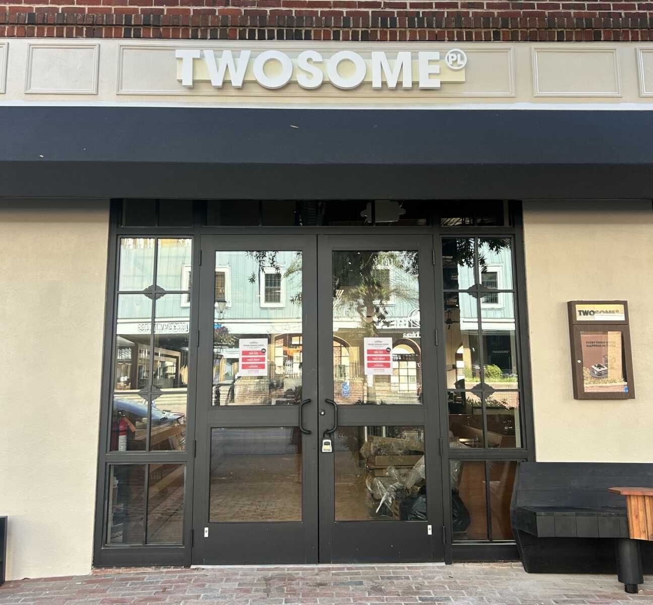Storefront with black-framed double glass doors under a dark blue awning; sign reads TWOSOME PL.