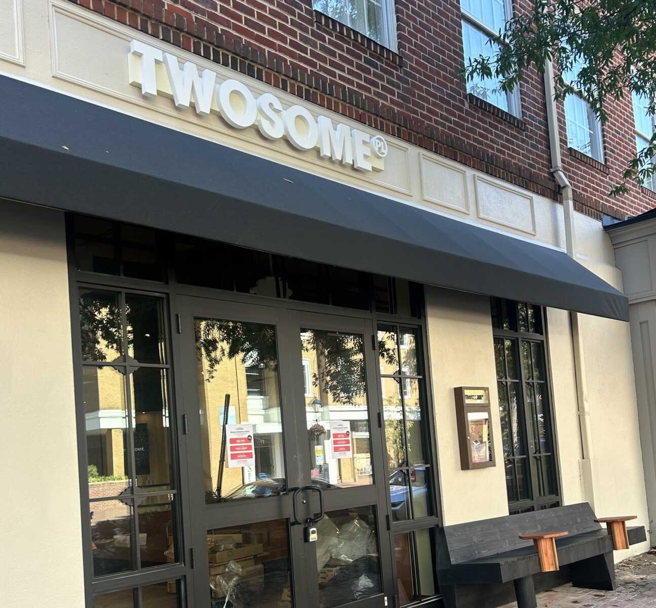 Exterior storefront with a dark gray awning, large glass doors, and a brick facade; a bold TWOSOME sign above the entrance.